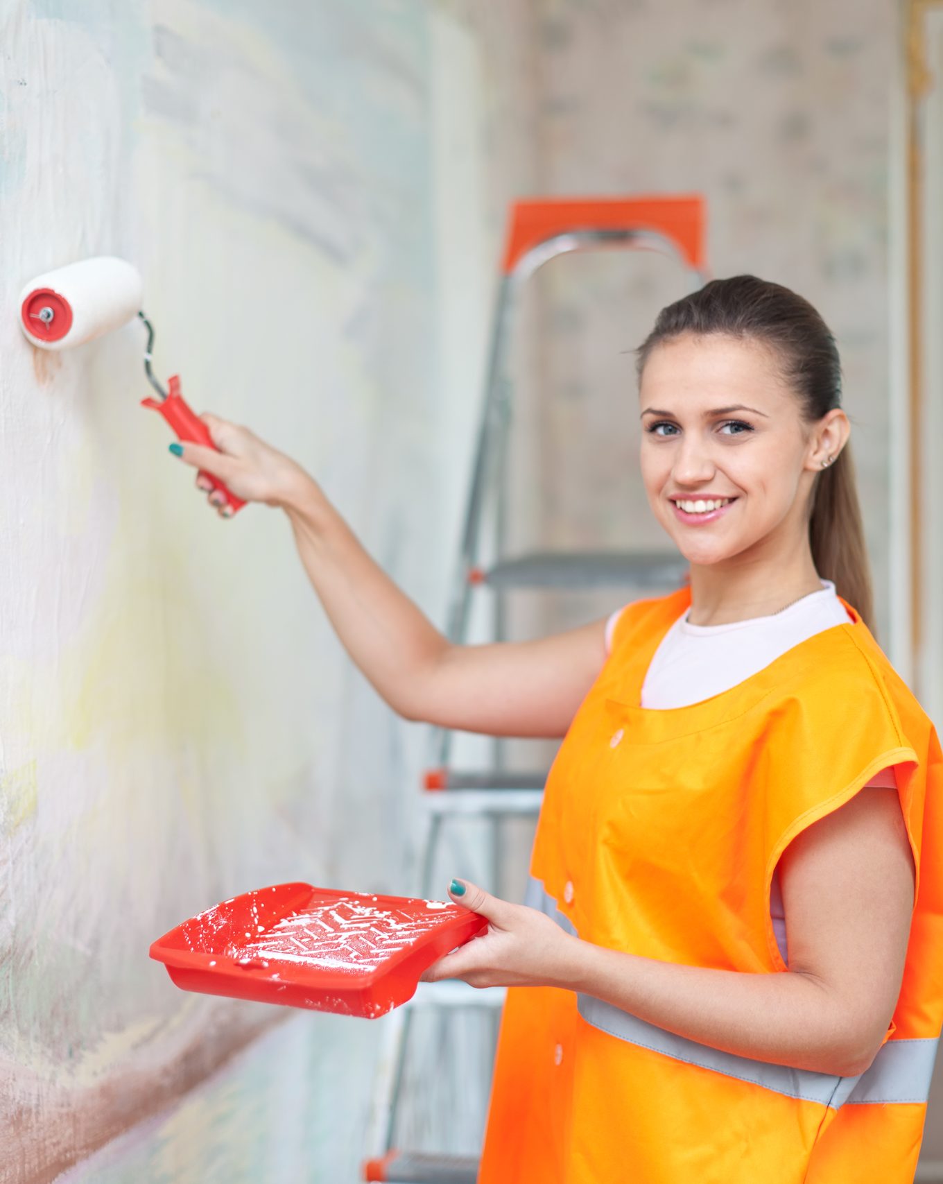 Female house painter paints wall with roller